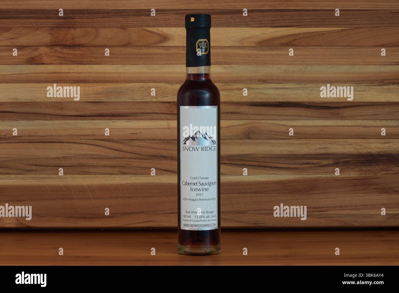 Eine Flasche Snow Ridge Cabernet Savignon Icewine, ein süßer kanadischer Dessertwein mit kaltem Klima, der aus Trauben hergestellt wird, die auf der Weinrebe auf einem rustikalen Holzhintergrund gefroren sind Stockfoto