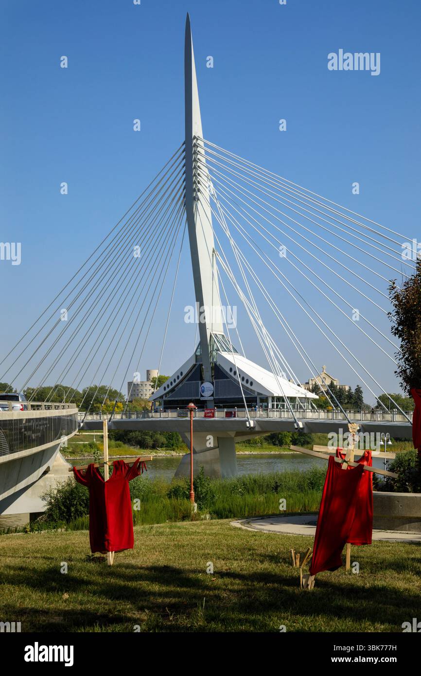 Rote Kleidung hängt vor der Fußgängerbrücke Esplanade Riel, die den Red River in der Innenstadt von Winnipeg, Manitoba, Kanada überquert Stockfoto