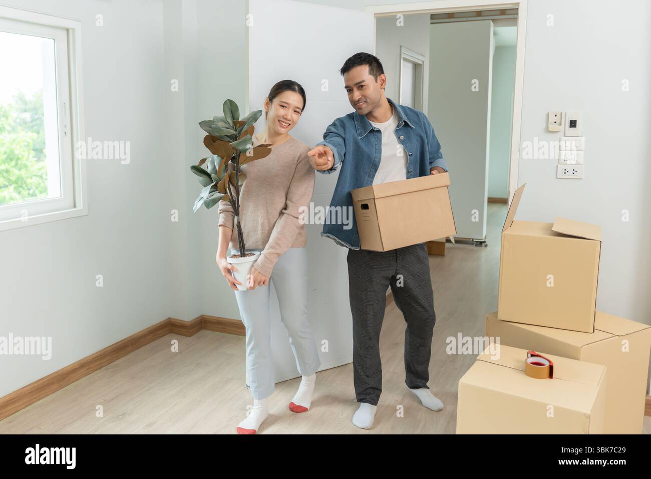Umzugshaus, Ehemann und Ehefrau halten Box und Möbel für eine neue Wohnung oder ein neues Zuhause, im Zimmer war eine Pappschachtel mit persönlichen Sachen und Stockfoto
