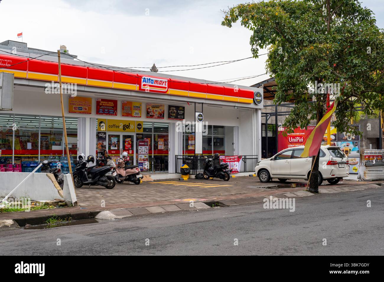 Bali, Indonesien - 25. Dezember 2024: Alfamart Supermarkt mit einem weißen Auto davor. Stockfoto