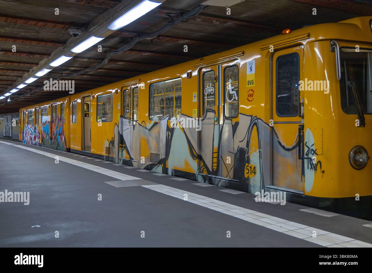 An einem Bahnsteig mit Deckenbeleuchtung steht ein gelber U-Bahn-Wagen mit lebendiger Graffiti-Kunst. Berlin, Deutschland. 28. März 2025. Stockfoto