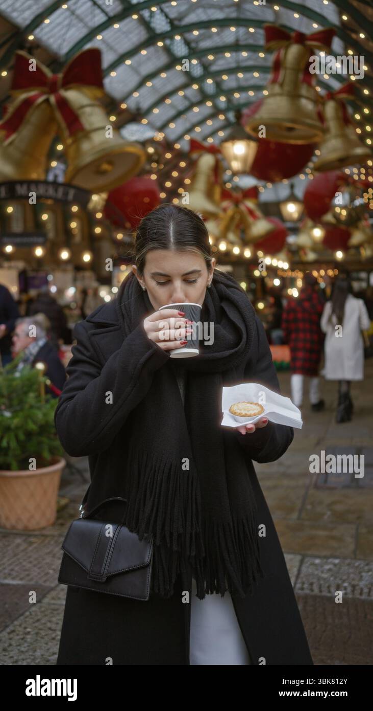 Frau genießt festliche Atmosphäre im london covent Garden mit weihnachtslichtern, die Kaffee und Gebäck unter verzierten Bögen halten. Stockfoto