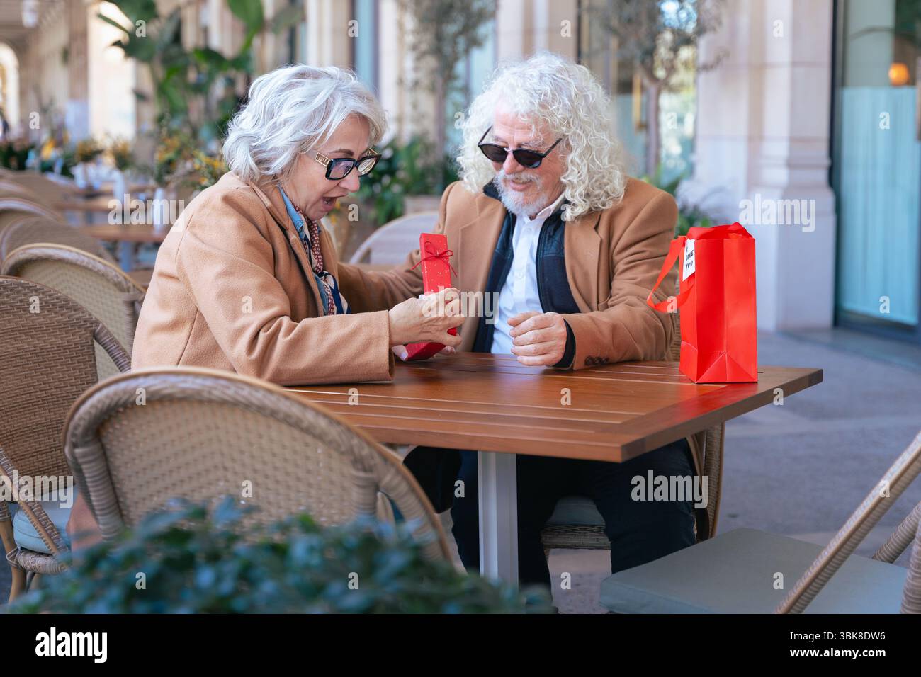Lächelndes Seniorenpaar genießt gemeinsam Kaffee im Café im Freien in lässigen Outfits Stockfoto