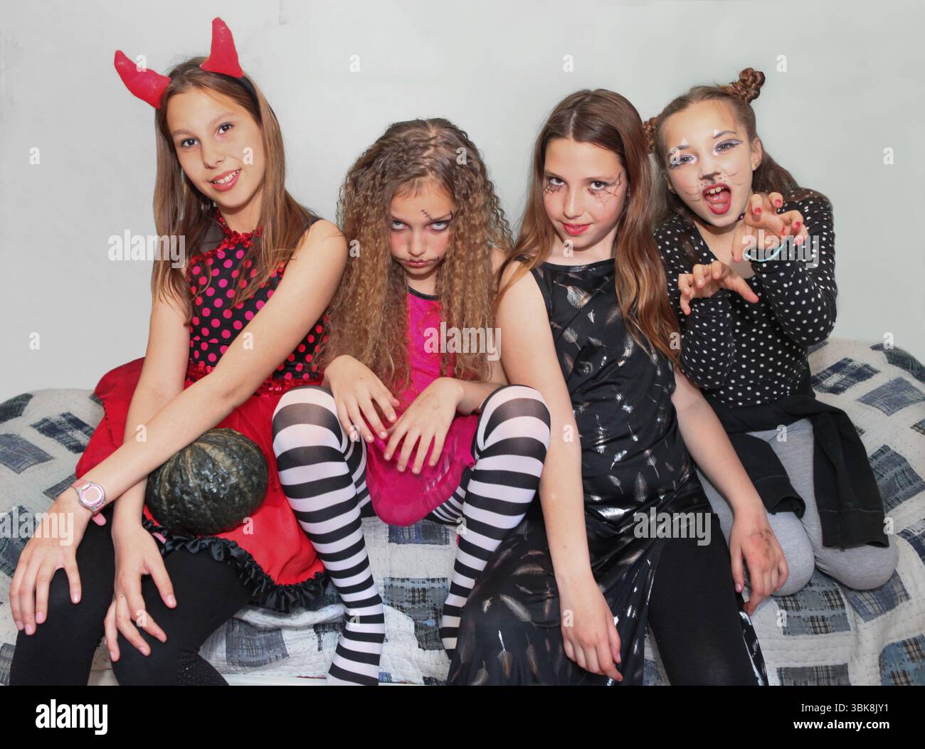 Vier junge Mädchen in farbenfrohen Halloween-Kostümen posieren drinnen, lächeln und blicken in die Kamera. Stockfoto