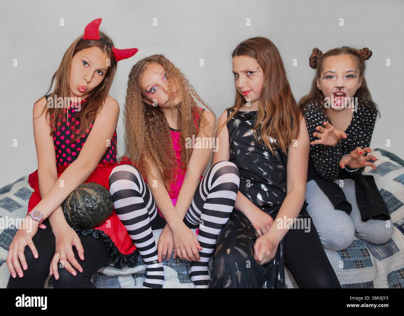Vier junge Mädchen in farbenfrohen Halloween-Kostümen posieren drinnen, lächeln und blicken in die Kamera. Stockfoto
