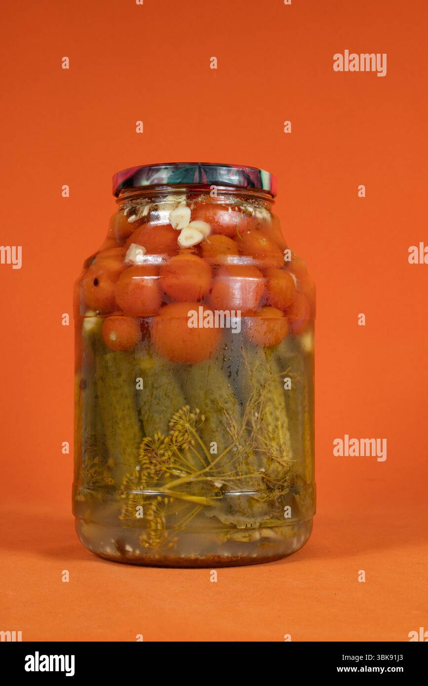 Hausgemachte eingelegte Dosentomaten und Gurken in einem Glas auf einem leuchtend orangen Hintergrund Stockfoto