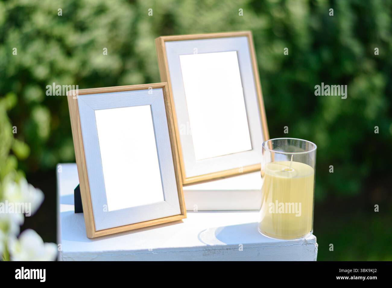 Eleganter hölzerner Bilderrahmen auf dem Buch mit Kerze auf weißem Ausstellungsstand vor der Hochzeit Stockfoto