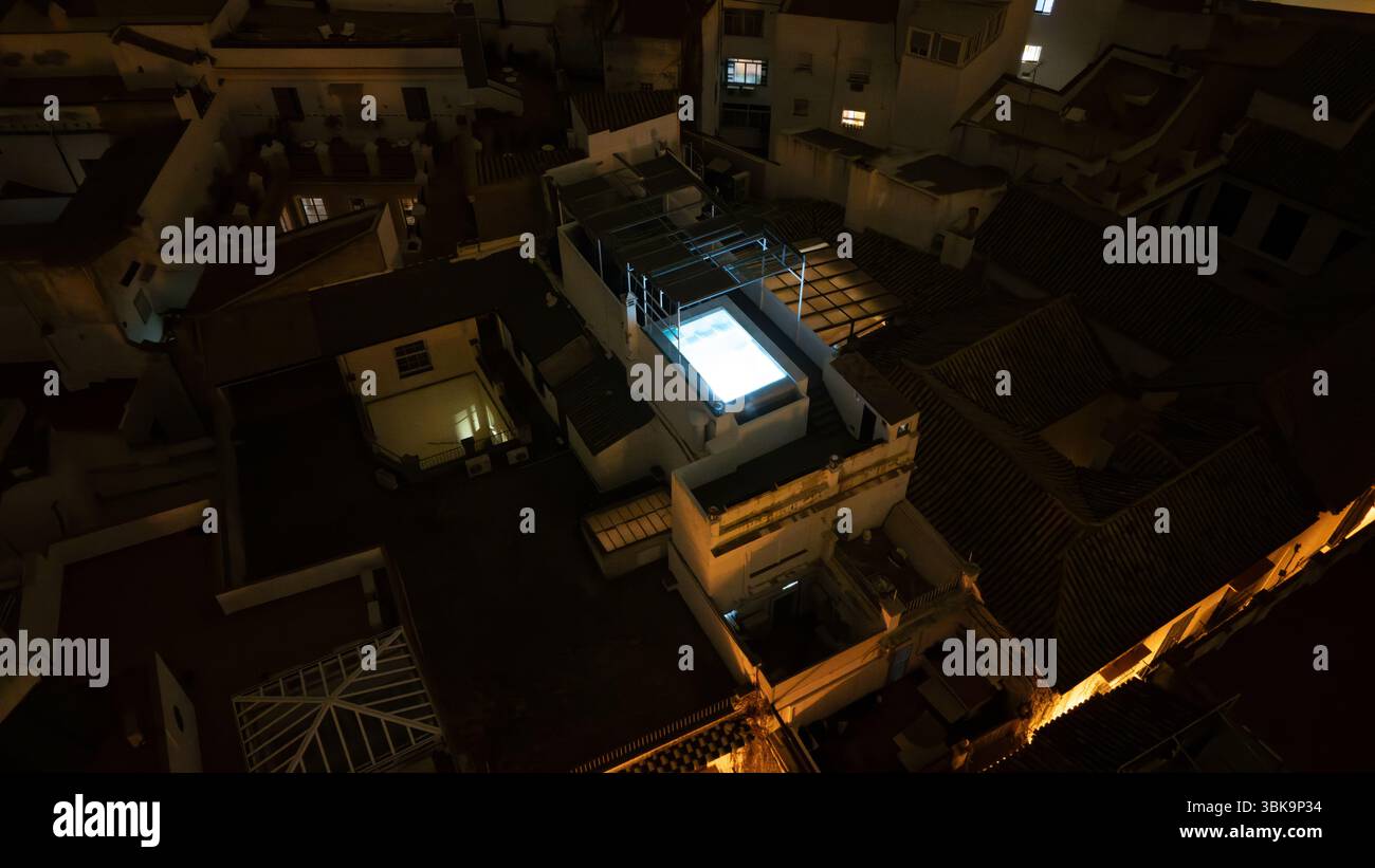 Blick aus der Vogelperspektive auf einen Pool auf dem Dach, beleuchtet bei Nacht in einer urbanen Umgebung. Stockfoto