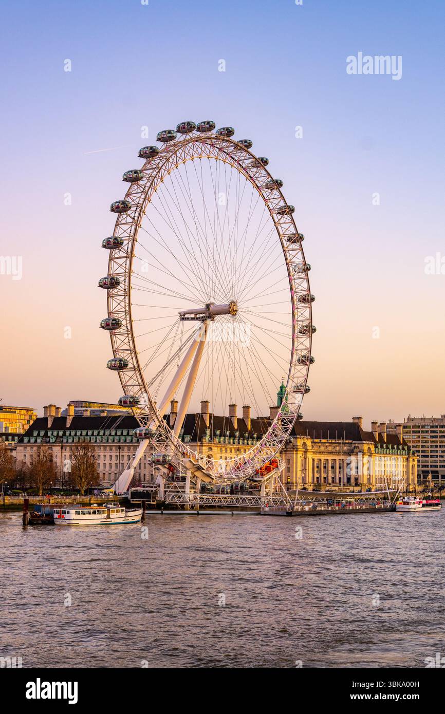 Das London Eye erhebt sich über dem South Bank und bietet einen atemberaubenden Blick auf die Stadt. Die Boote gleiten sanft entlang der Themse, während sich die Dämmerung einsetzt, und schaffen eine malerische Umgebung. Stockfoto