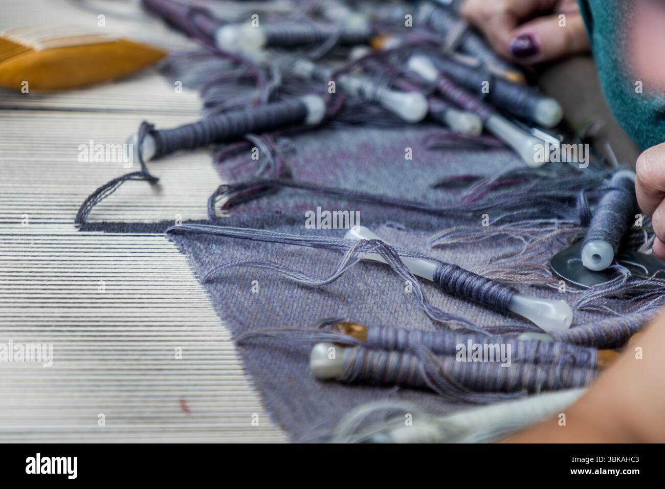Atelier Robert Four in Aubusson, wo der Wandteppich Hommage à George Sand hergestellt wird. Nahaufnahme des Shuttles mit Wollgarn in verschiedenen Farben und ein Abschnitt der Kette, die straffen Längsfäden im Webstuhl, durch die das Shuttlegarn mit dem Schussfaden geführt wird. Rue Madeleine, Aubusson, Nouvelle-Aquitaine, Frankreich Stockfoto