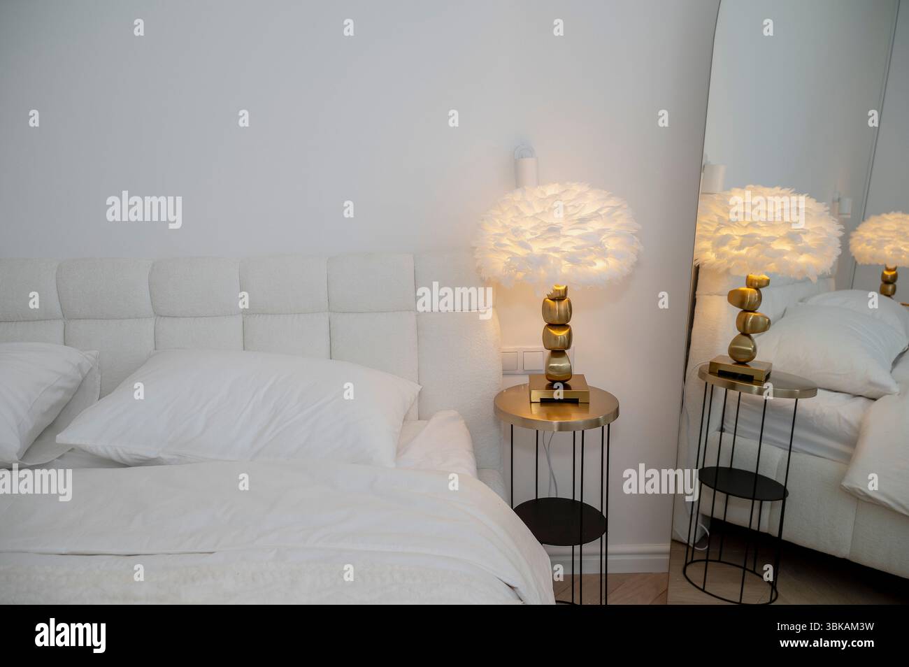 Inneneinrichtung des Schlafzimmers mit moderner Leselampe auf dem Tisch neben dem Doppelbett mit Kissen. Stockfoto