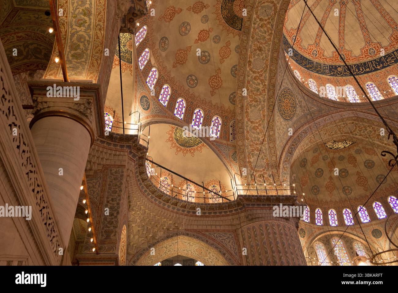 Besucher bewundern die atemberaubende Innenarchitektur und die kunstvolle Dekoration einer historischen Moschee in Istanbul mit leuchtendem Buntglas. Stockfoto