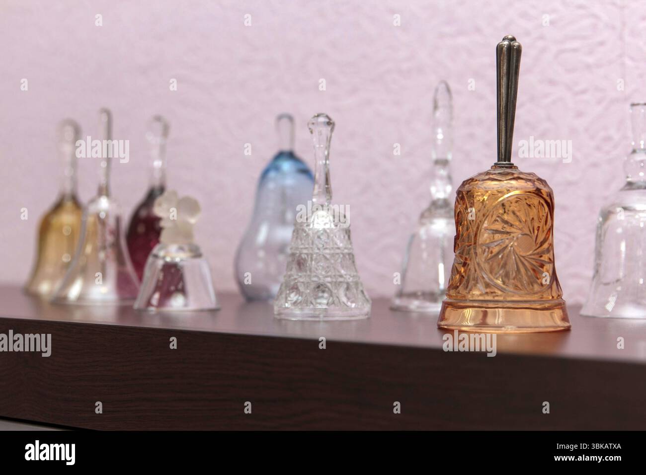 Verschiedene transparente und farbige Glasglocken, die auf einem dunklen Holzregal an einer strukturierten Wand angeordnet sind und eine Kollektion von Wohnkultur zeigen Stockfoto