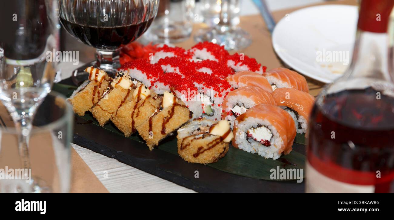 Eine Auswahl an Sushi-Brötchen, darunter gebratene, Lachs und Reh, serviert auf Schieferteller mit Rotwein auf festlichem Innentisch Stockfoto