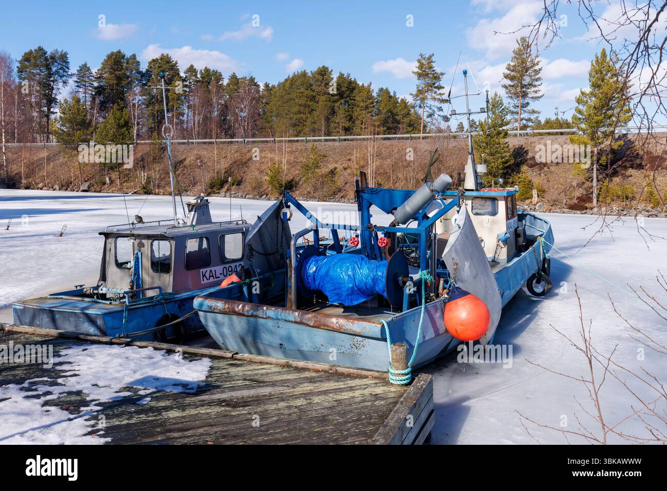 Kleine Binnenfischtrawler ankerten und stecken im Eis im Frühling am Jachthafen Kivisalmi, See Etelä-Konnevesi, Finnland Stockfoto