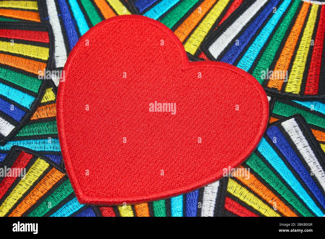 Großes, rot gesticktes Herz auf farbenfrohem Textilhintergrund. Symbol für Liebe, Romantik, Hochzeiten und handgefertigtes Kunsthandwerk. Stockfoto