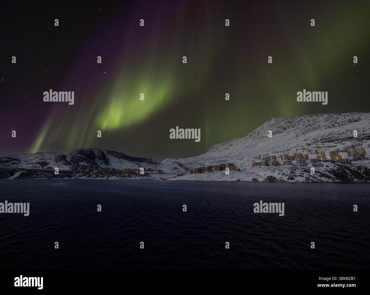 Nordlichter über der Küstenstadt Nuuk, Grönland, mit schneebedeckten Gebäuden und Bergen im Winter. Die Aurora wird am arktischen Nachthimmel durchbogen. Stockfoto