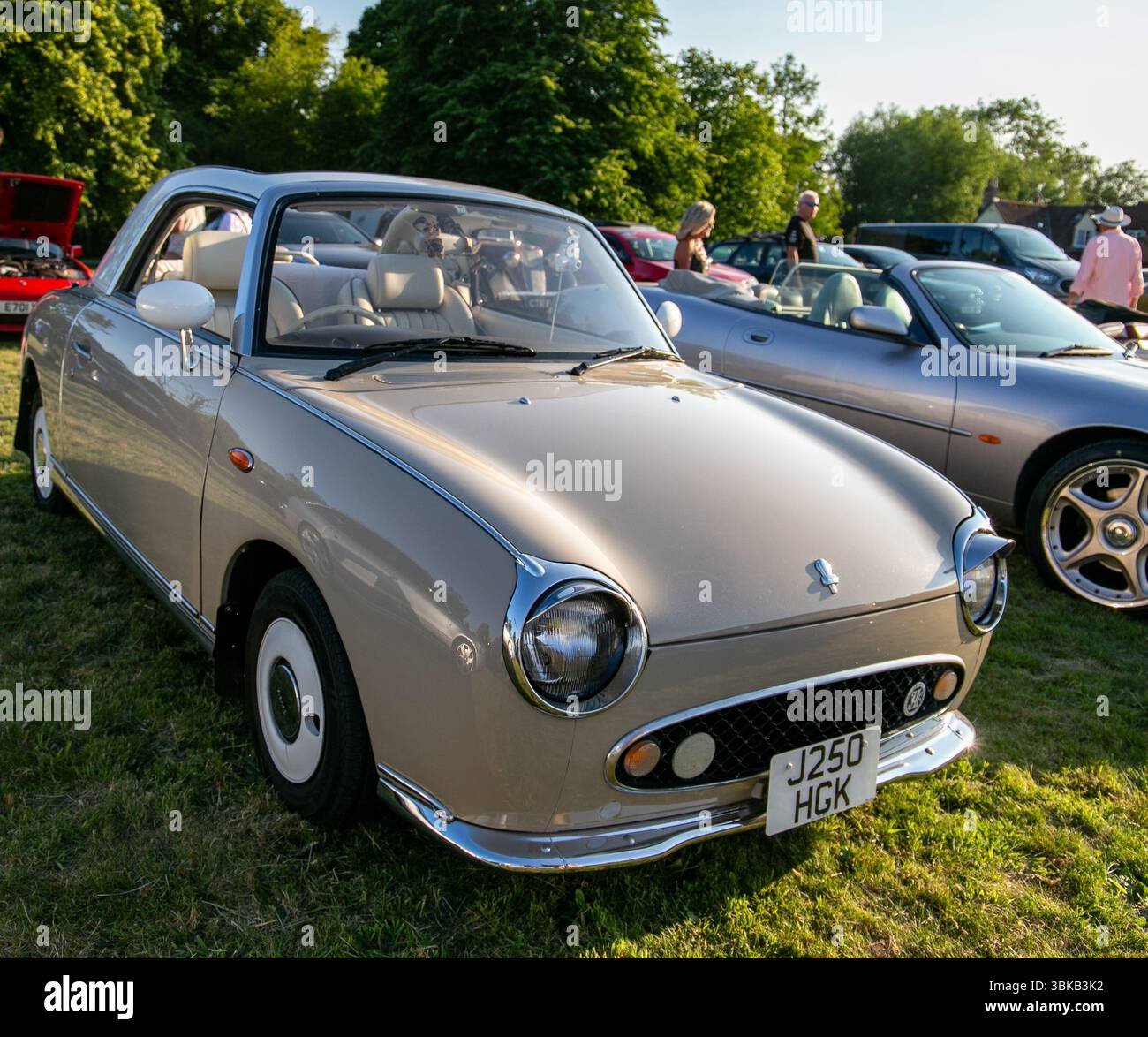 Creme Nissan Figaro Cabriolet auf Gras geparkt, präsentiert bei einem Oldtimer-Event mit mehreren anderen Autos im Hintergrund Poulshot Devizes UK Stockfoto