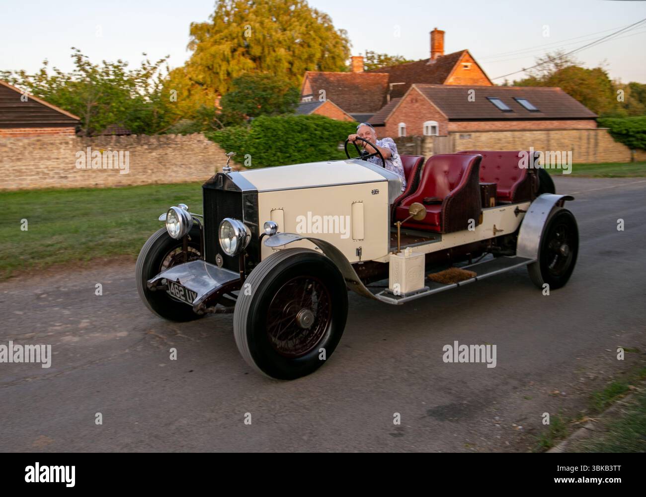 Vintage Rolls-Royce 20/25 Auto mit roten Ledersitzen auf einer Landstraße vorbei an einem Backsteinhaus, umgeben von Grün und Abendlicht Stockfoto