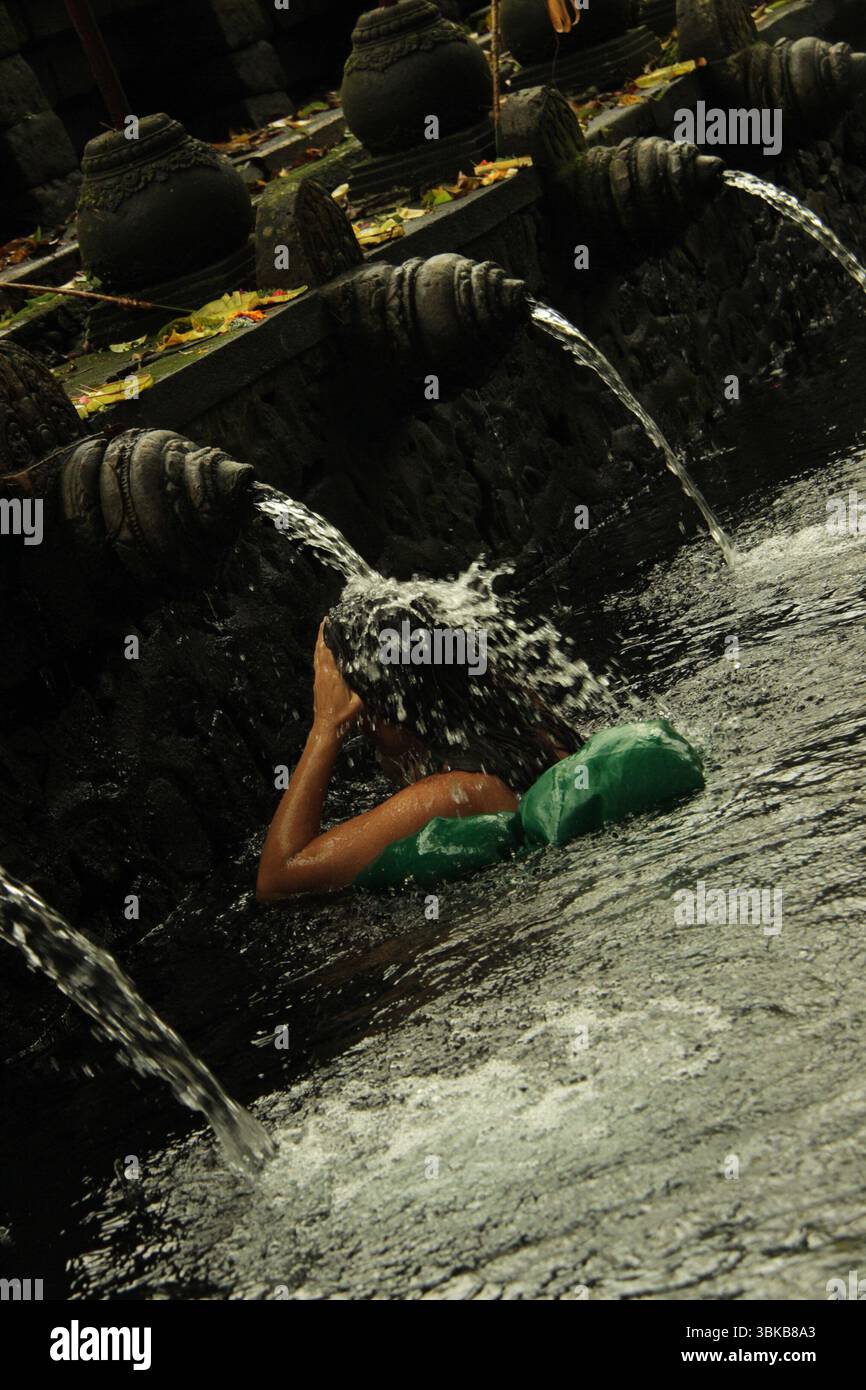 Spirituelles Ritual, heiliges Wasser, Tempel auf Bali – Eine Frau führt ein Reinigungsritual im Tirta Empul Tempel durch, umgeben von heiligen Brunnen und einem My Stockfoto