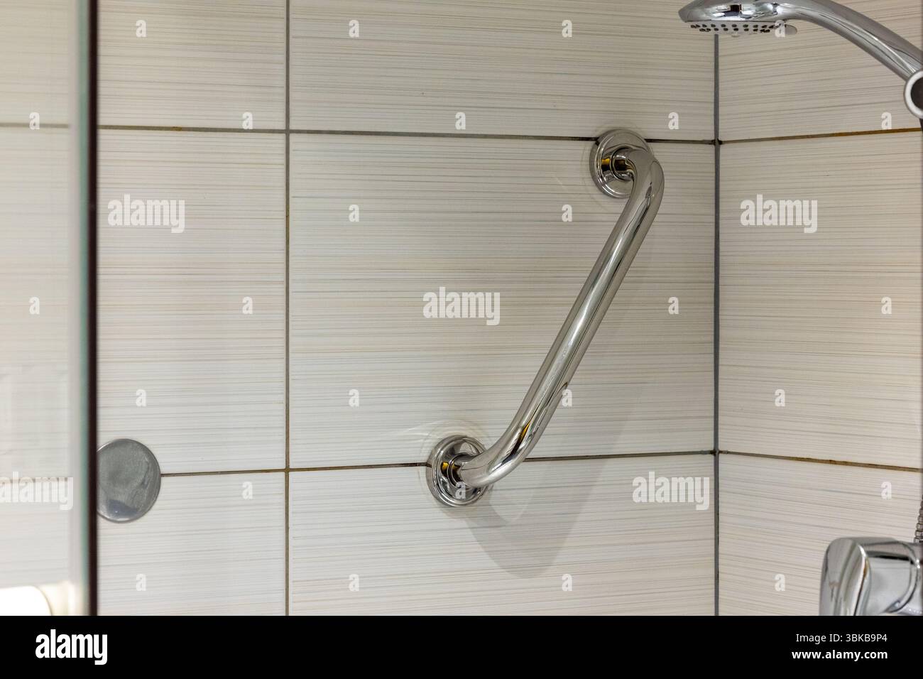 Verchromter Badezimmergriff an der Wand in der Duschkabine. Badezimmer mit hellen Keramikfliesen Stockfoto