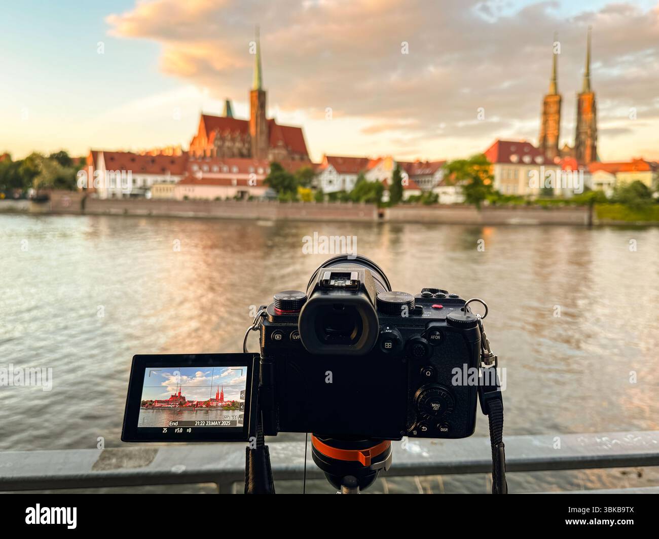 Eine Digitalkamera auf einem Stativ, die ein atemberaubendes historisches Stadtbild bei einem malerischen Sonnenuntergang entlang eines Flusses fotografiert und dabei die Fotografie als Kunst und Kunst betont Stockfoto