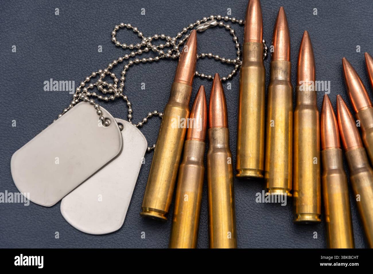 Militärische Hundeanhänger (Soldatenanhänger) und einige Gewehrpatronen liegen auf einer dunklen strukturierten Oberfläche Stockfoto