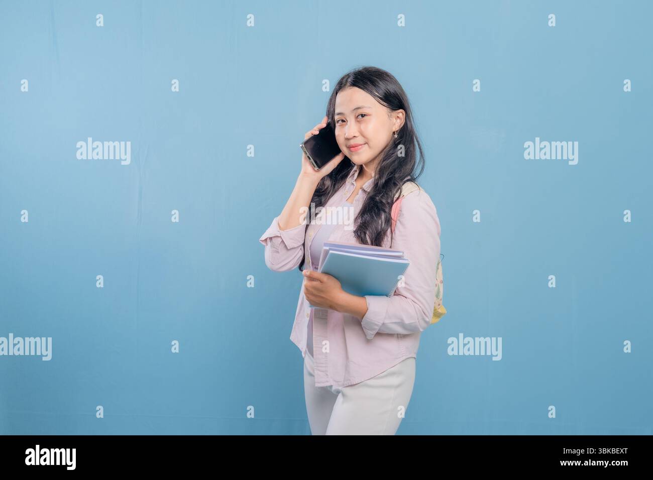 Eine Frau redet auf ihrem Handy, während sie einen Stapel Bücher hält. Sie lächelt und ist gut gelaunt Stockfoto