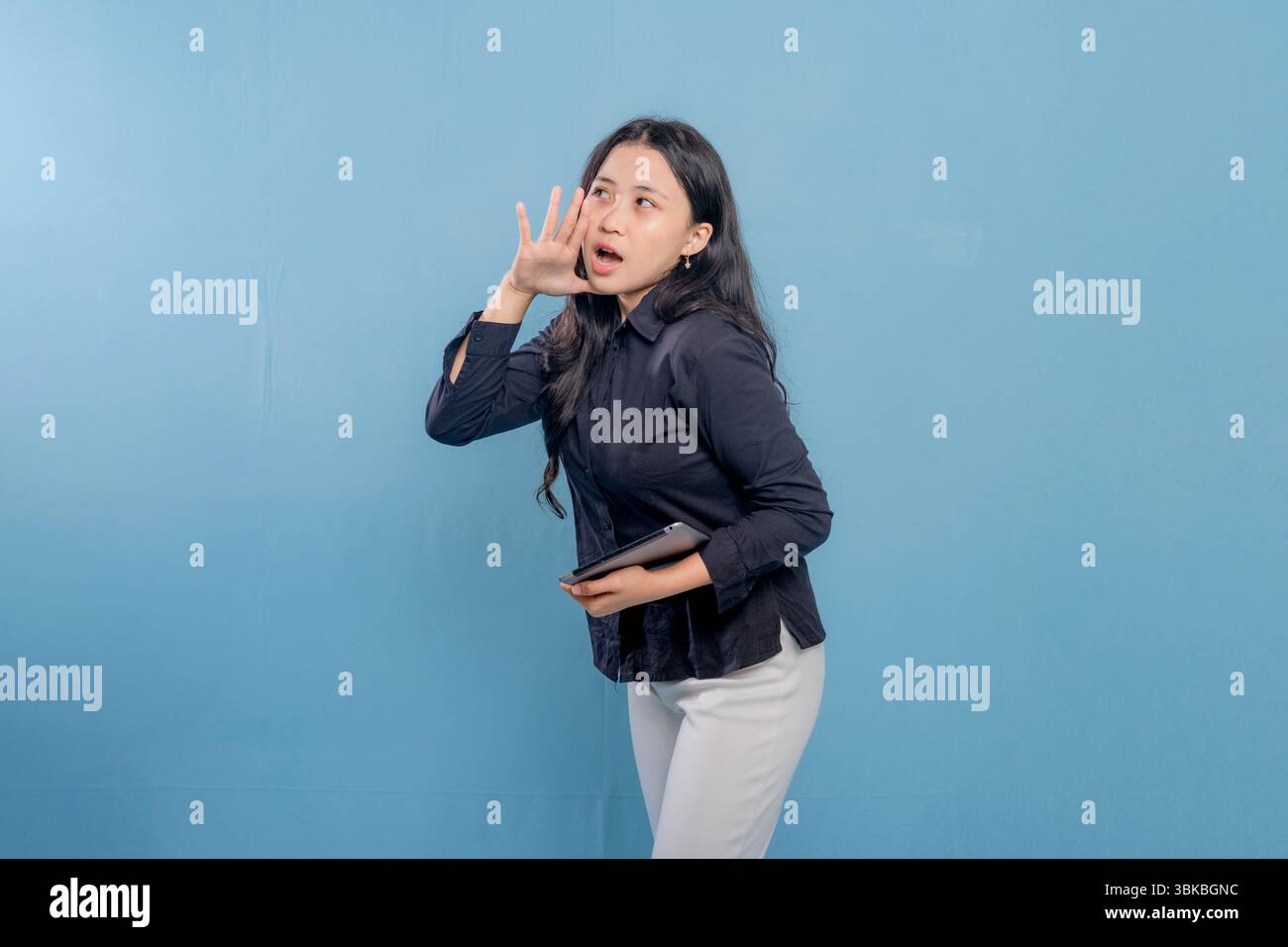 Eine Frau in einem schwarzen Hemd und einer weißen Hose hält eine Tablette in der Hand. Sie blickt in die Kamera und macht ein lautes Geräusch Stockfoto