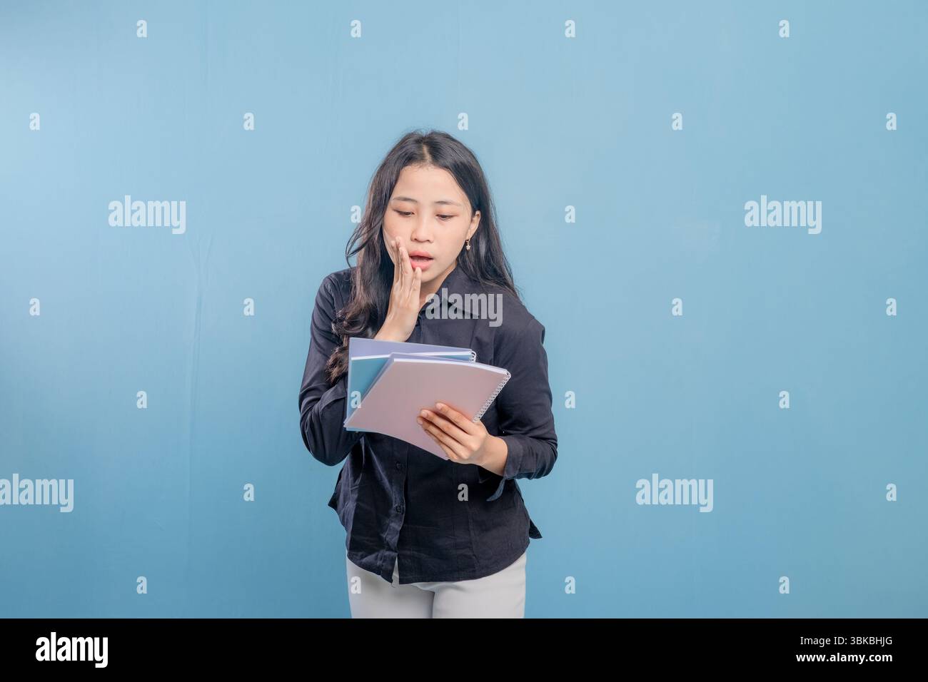 Eine Frau liest ein Buch, während sie in die Kamera schaut. Sie ist überrascht oder schockiert von etwas, das sie liest Stockfoto