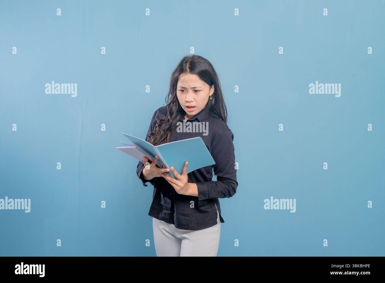 Eine Frau liest ein Buch, während sie in die Kamera schaut. Sie ist überrascht oder schockiert von etwas, das sie liest Stockfoto