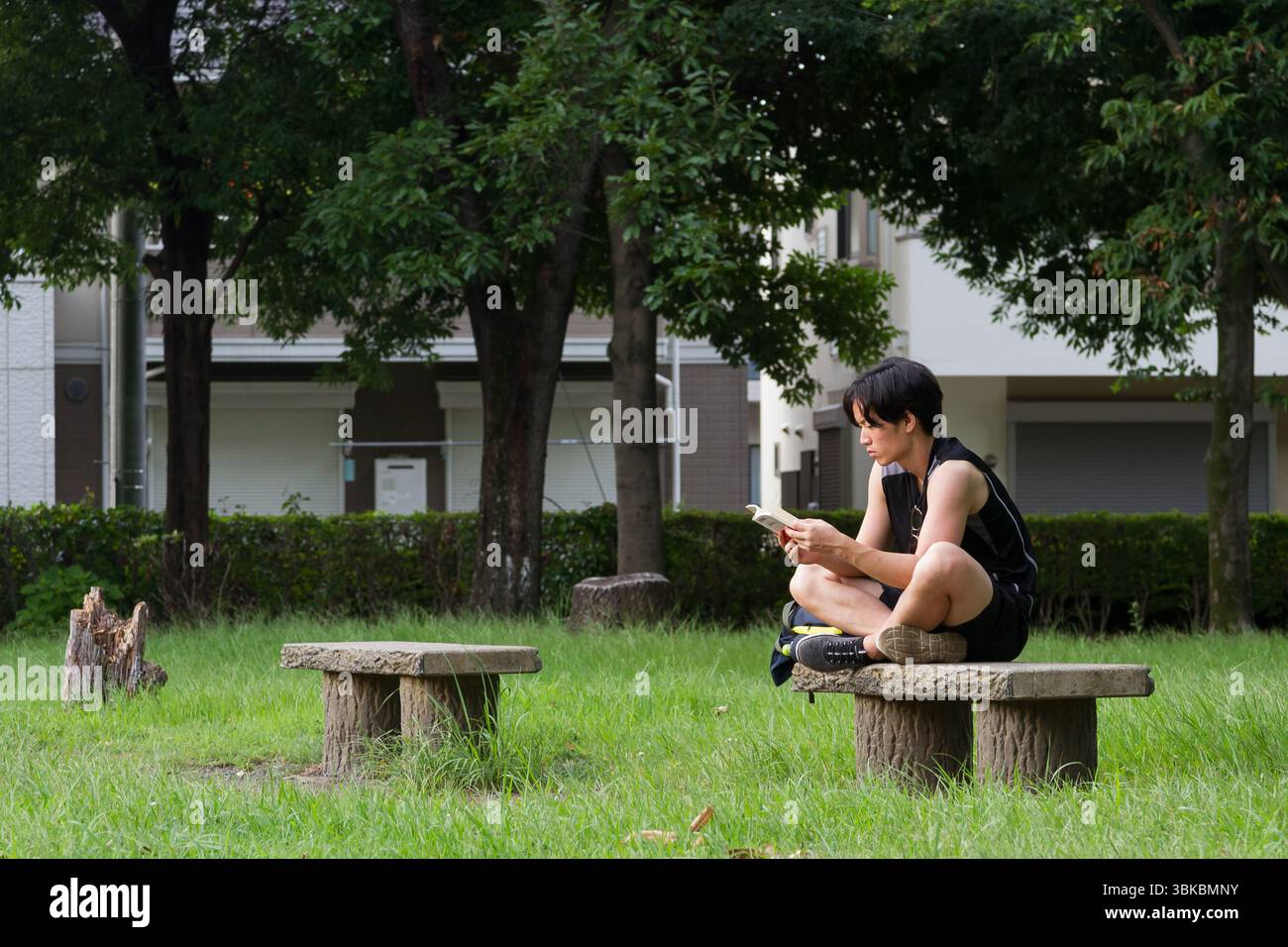 Ein junger Japaner sitzt auf einer kleinen Parkbank und liest ein Buch im ländlichen Kanagawa, Japan. Stockfoto