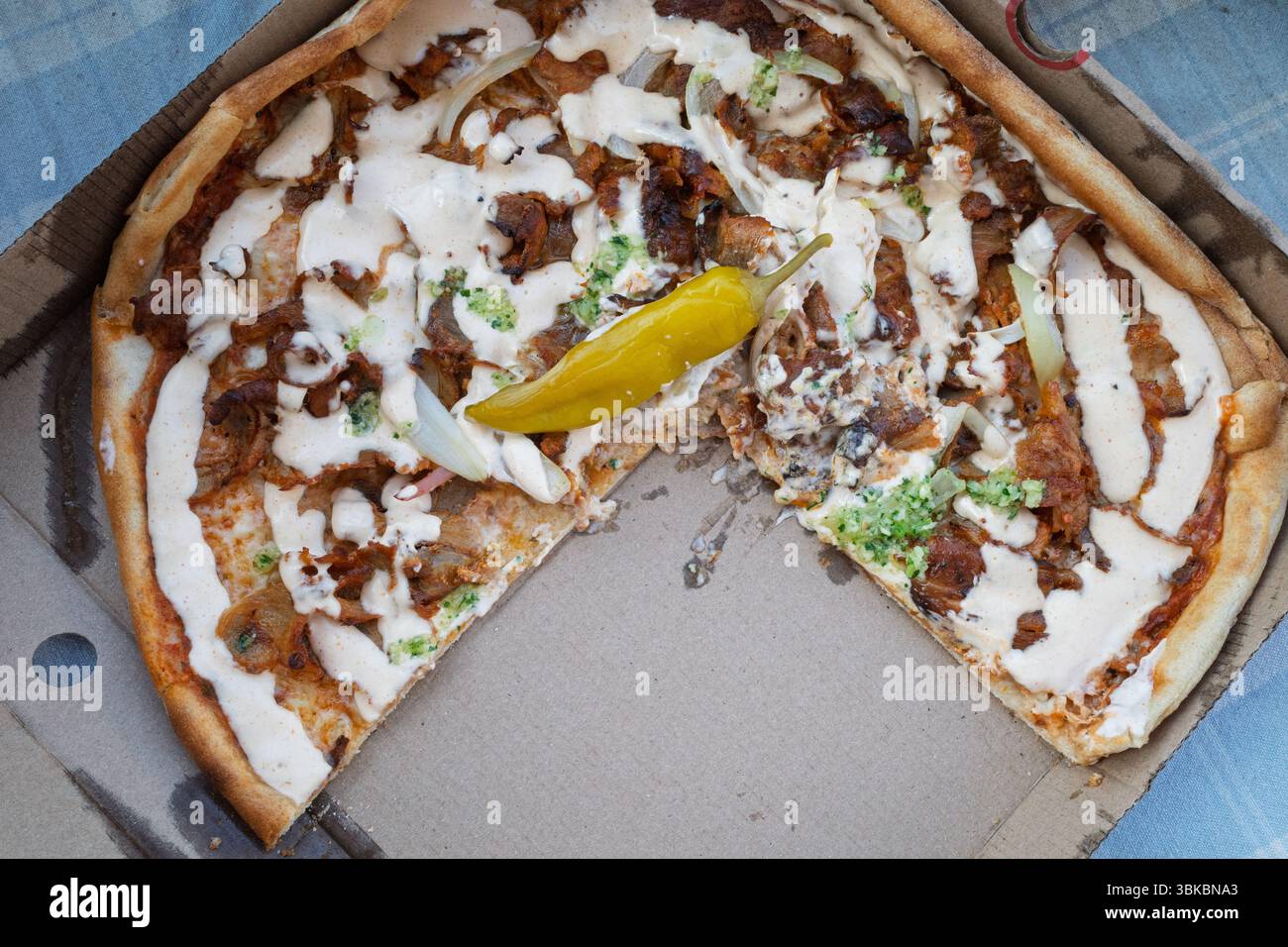 Eine halbgefressene Döner-Pizza, cremige Sauce, mit einem würzigen, eingelegten Pfeffer, der immer noch verlockend in der Box ist. Stockfoto