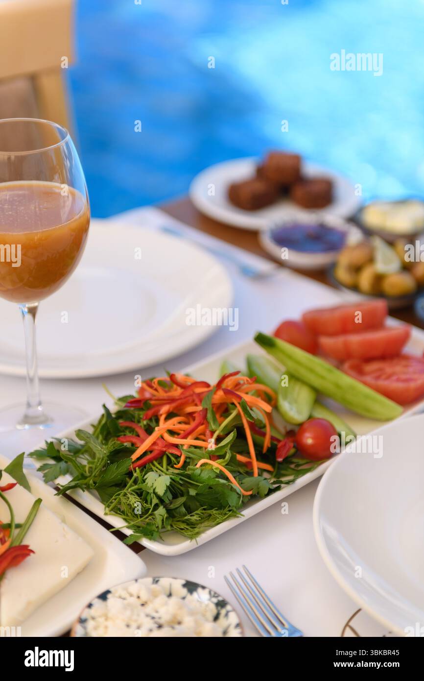 Ein großer Teller Salat mit Pfirsichsaft und Keksen auf einem Holztisch, mit einem Pool und einer Ecke eines Holzstuhls im Hintergrund. Stockfoto