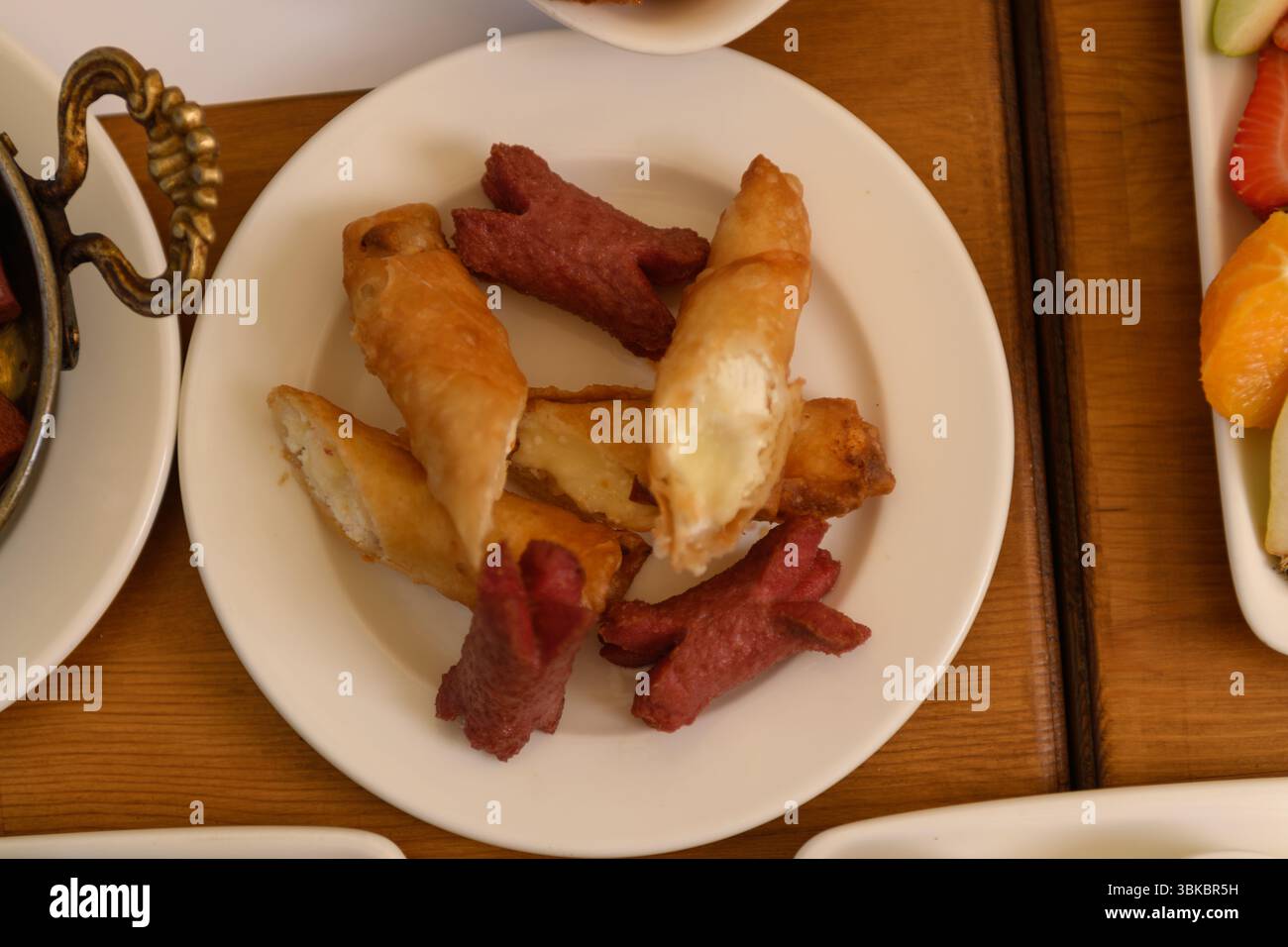 Ein Holztisch von oben mit einem Teller mit Bratwürsten und knusprigen Käsestäbchen, Teil einer Hotelfrühstücksszene. Stockfoto
