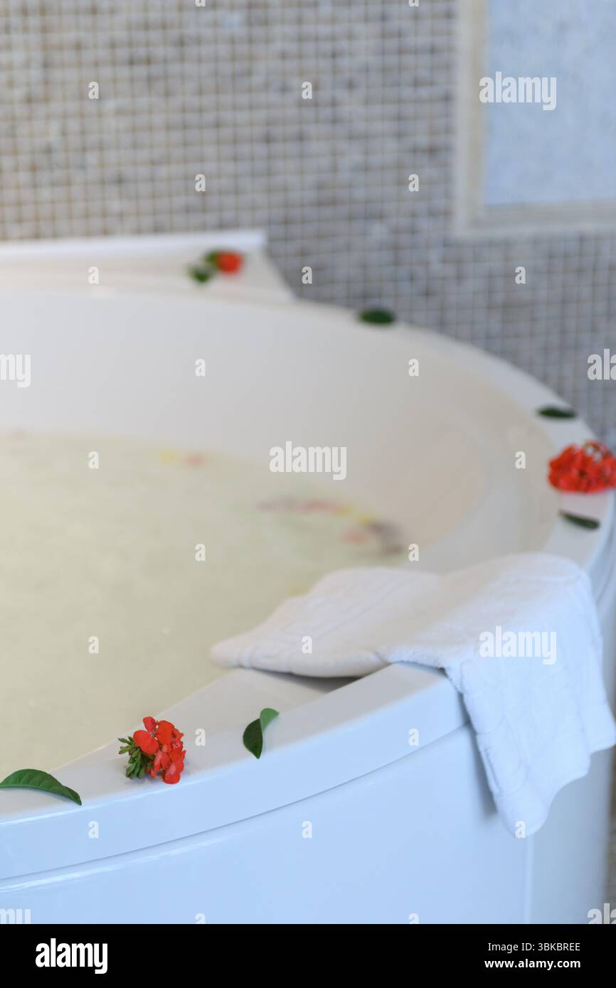Entspannender Jacuzzi mit Schaum und verstreuten Rosen für eine luxuriöse und romantische Atmosphäre. Stockfoto