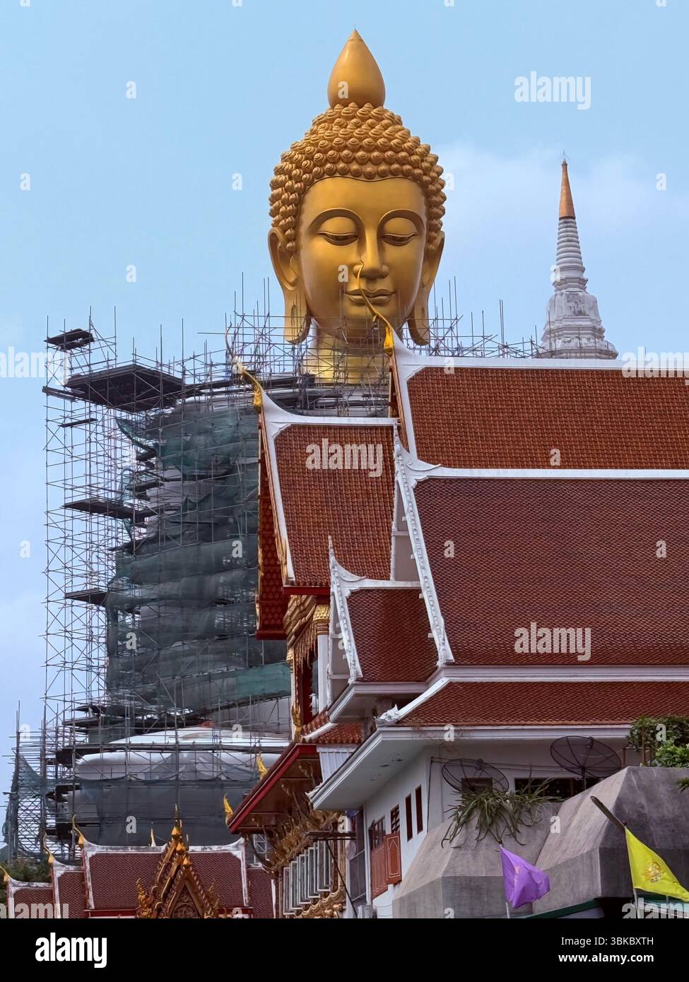 Ein majestätischer goldener Buddha erhebt sich über Tempeldächern und Gerüsten in Thailand und symbolisiert Ehrfurcht inmitten von Transformation und Erneuerung. - Smartphone-aufgenommenes Stockfoto