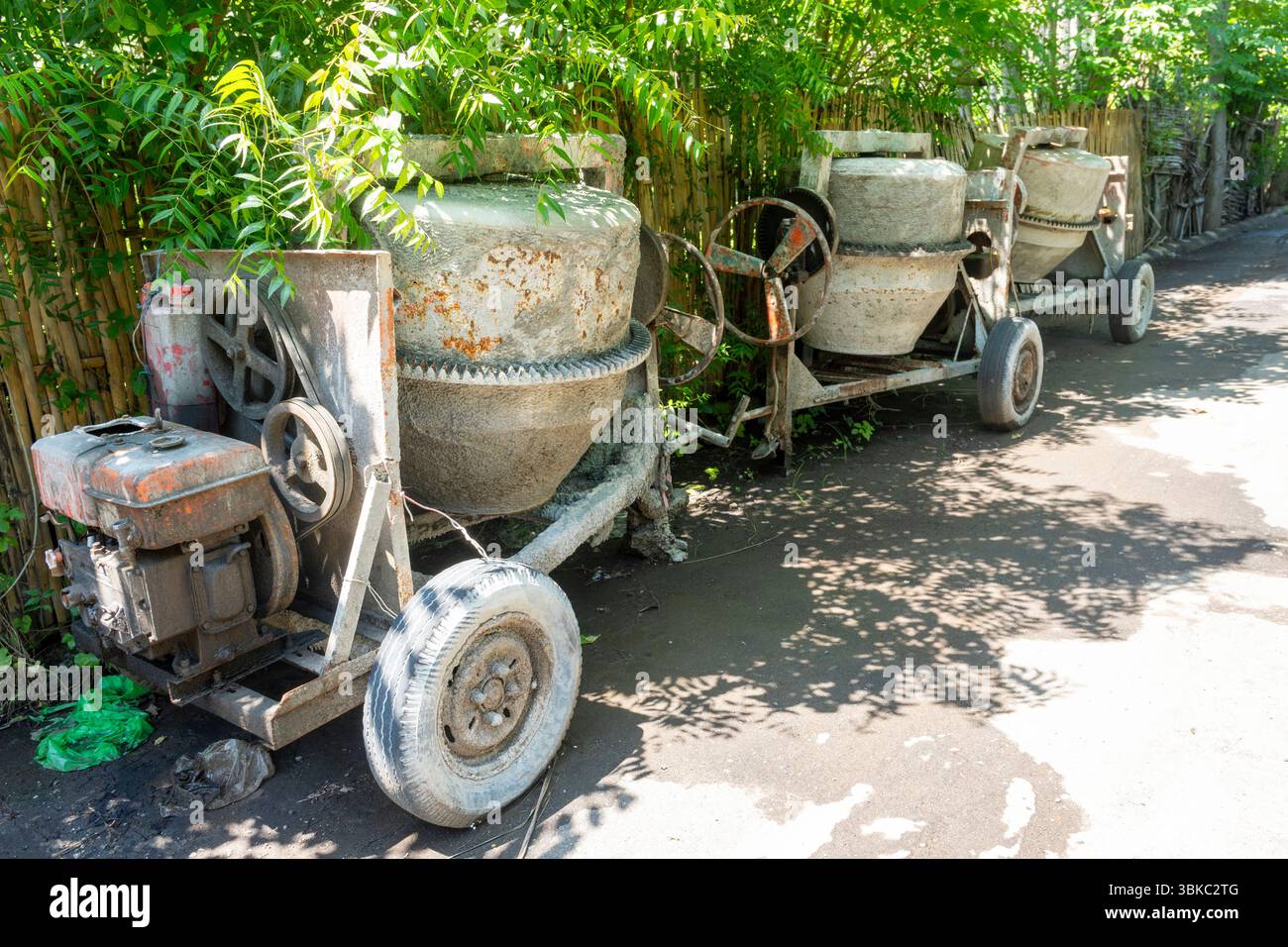 Zementmischer mit rostigem Rad sitzt in einem Hof. Das Rad fehlt, und die Maschine befindet sich in einem Defekt Stockfoto