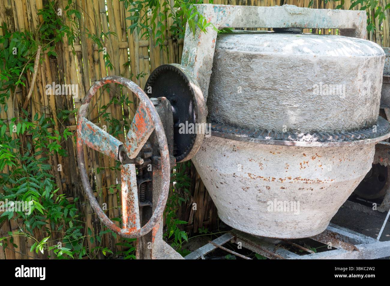 Zementmischer mit rostigem Rad sitzt in einem Hof. Das Rad fehlt, und die Maschine befindet sich in einem Defekt Stockfoto