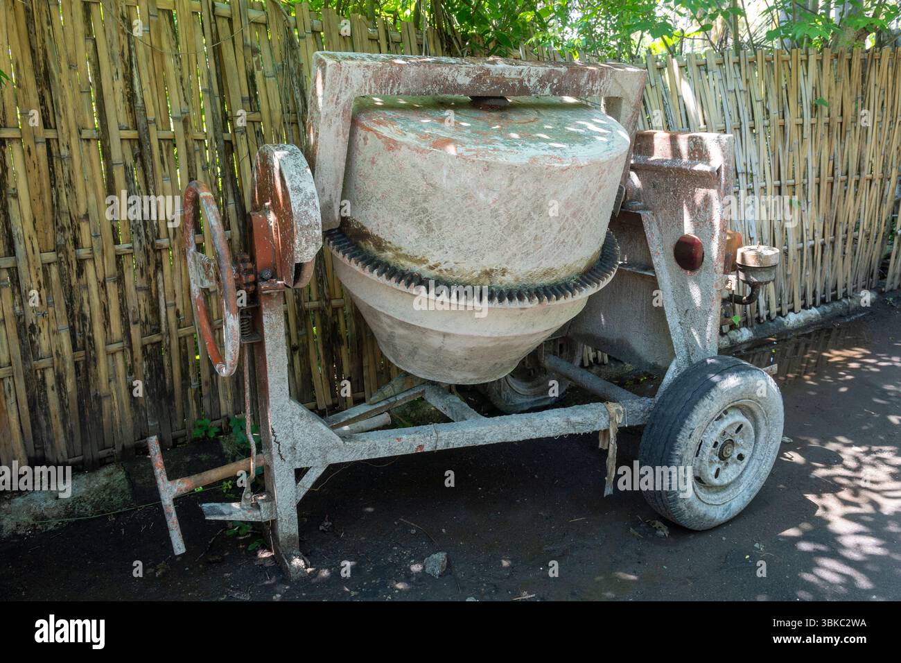 Zementmischer mit rostigem Rad sitzt in einem Hof. Das Rad fehlt, und die Maschine befindet sich in einem Defekt Stockfoto