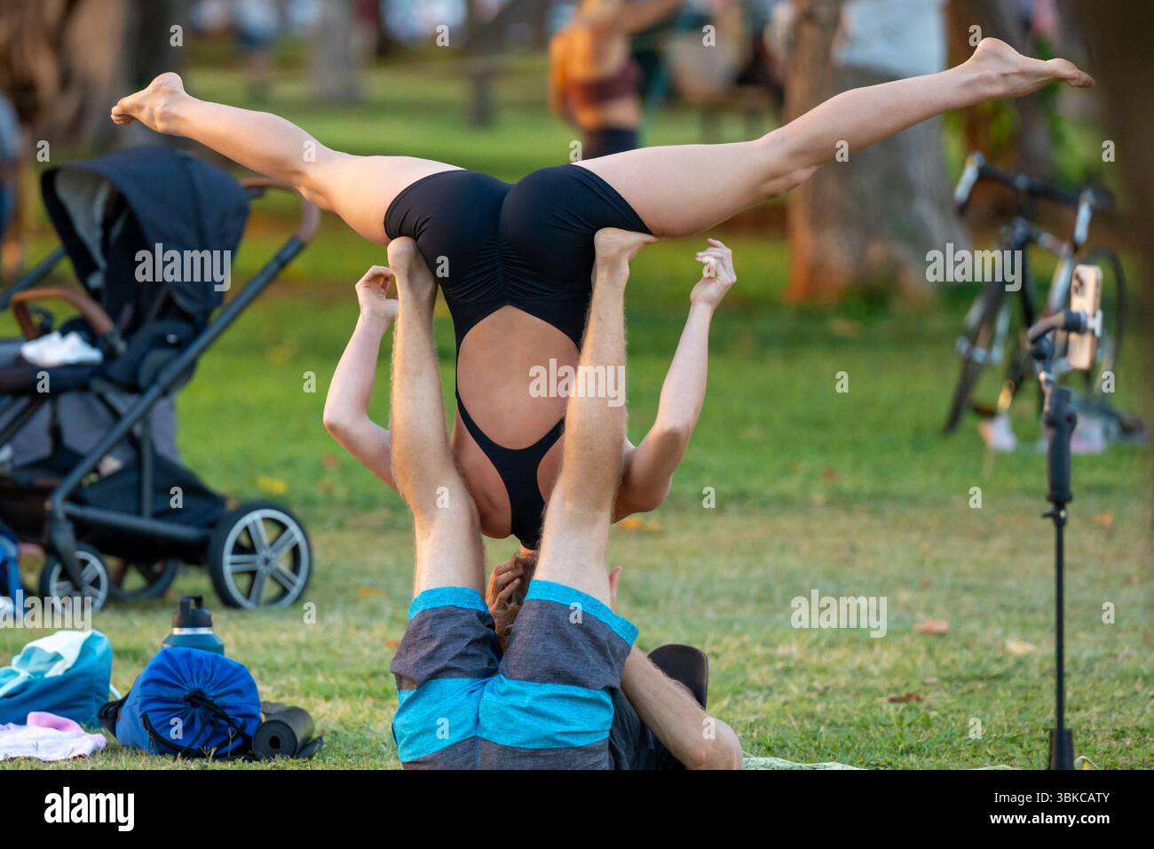 Ein Paar spielt eine Acro-Yoga-Pose in einem sonnendurchfluteten Park, wobei es Kraft und Gelassenheit vor einer natürlichen Kulisse im Freien ausgleicht. Unity, Wellness und Connectio Stockfoto