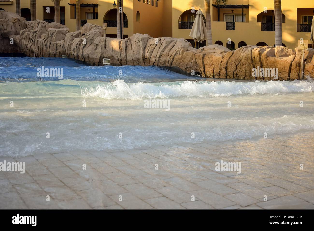 Wasserattraktion im Innenhof eines gemütlichen ägyptischen Hotels mit Palmen. Transparentes, sauberes Wasser, das sich künstlichen Wellen nähert. Östliche Architektur. Ideale pla Stockfoto