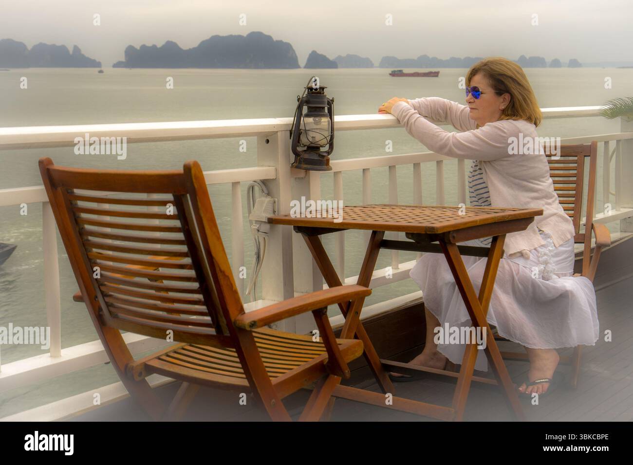 Lady in Shades sitzt an Deck des Bootes mit Blick auf die Ha Long Bay Stockfoto