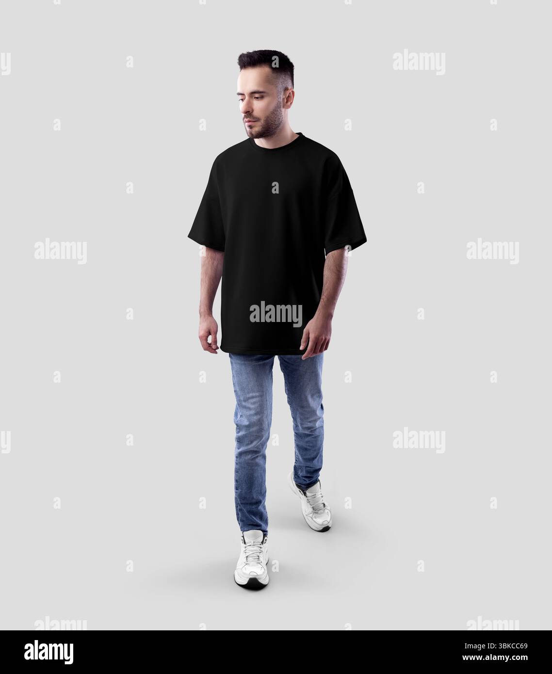 Modell eines schwarzen Oversize-T-Shirts auf einem bärtigen Walking Guy in Jeans, Sneakers, durchgehender Vorderansicht, Designbekleidung, Branding. Produktfoto Stockfoto