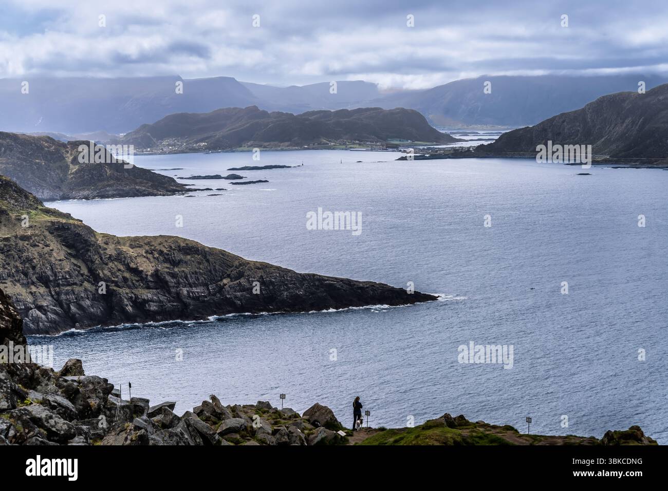 Atemberaubende Küstenlandschaft mit zerklüfteten Klippen, ruhigem Wasser und einer bergigen Kulisse unter einem bewölkten Himmel, die ein ruhiges und natürliches Atmo schafft Stockfoto