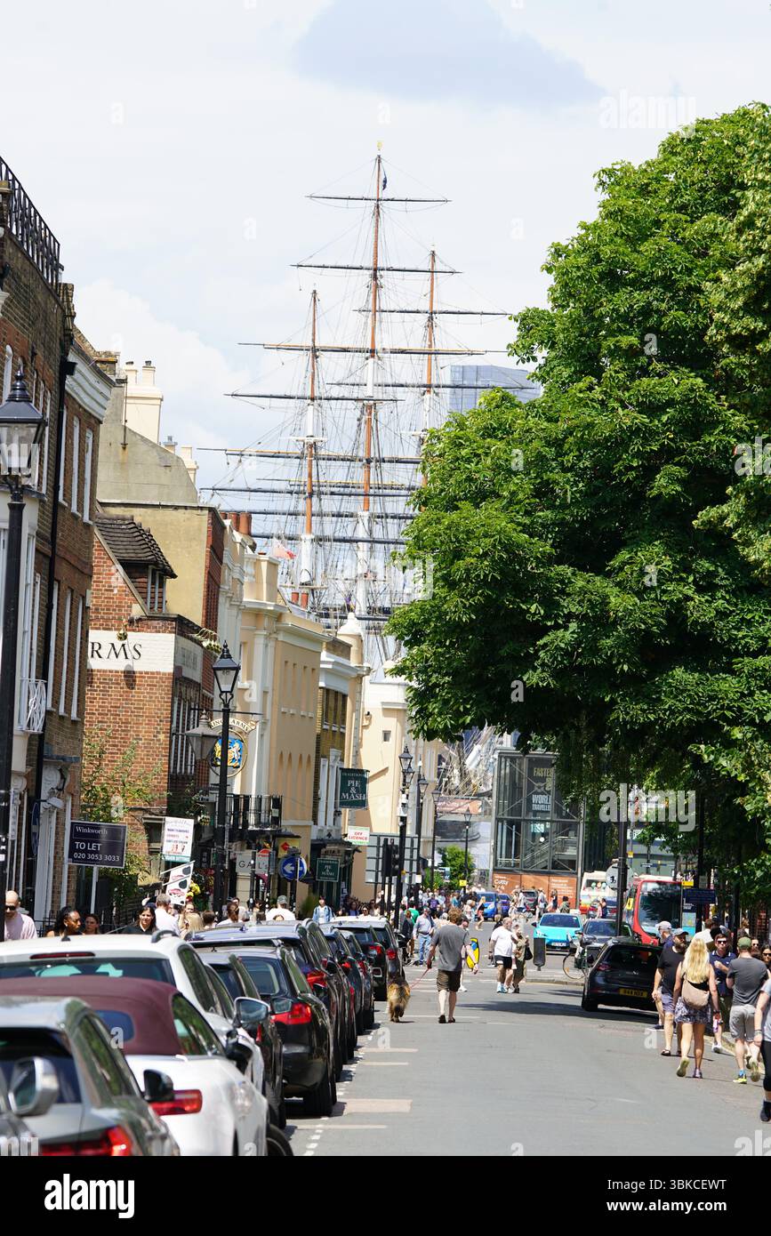 Geschäftige Straßenszene mit historischem Schiff und vorbeiziehenden Leuten. Greenwich, London, England Stockfoto