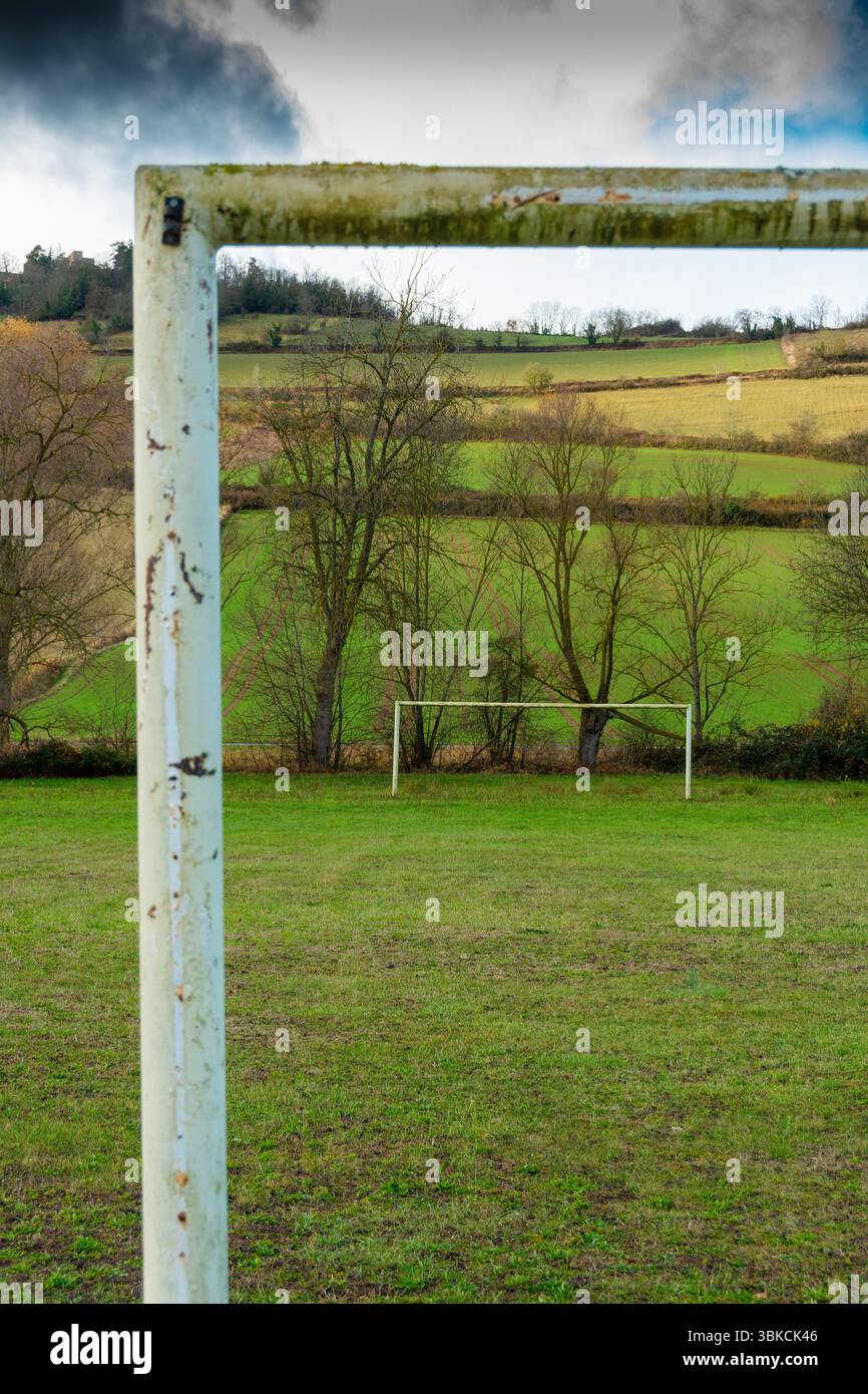 Ein verwitterter Fußball-Torpfosten steht im Vordergrund eines breiten grasbewachsenen Feldes mit üppig grünen Hügeln und Bäumen im Hintergrund. Auvergne. Frankreich Stockfoto