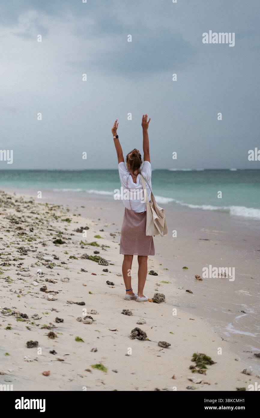 Junge Frau, die mit erhobenen Armen am felsigen tropischen Strand steht Stockfoto