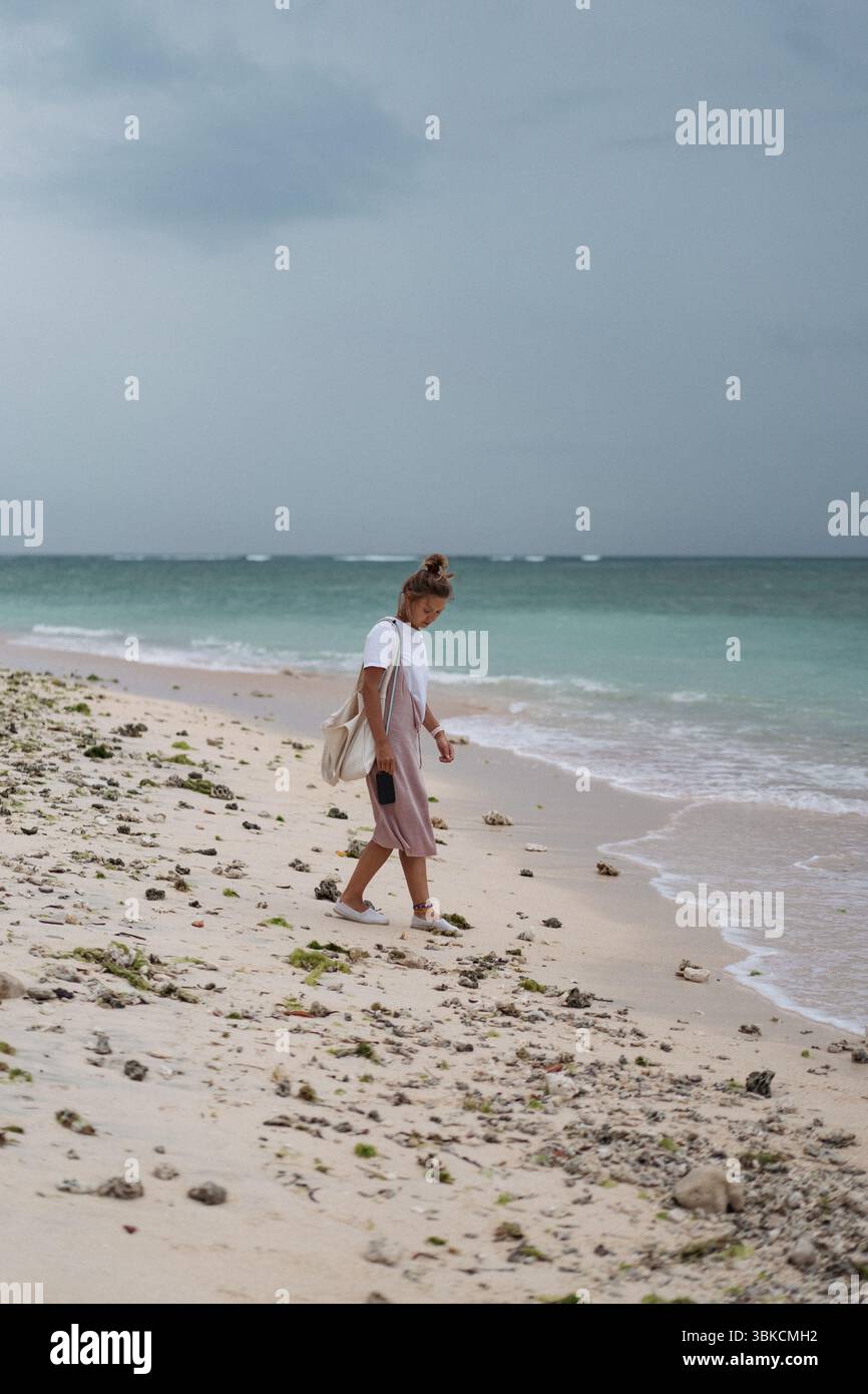 Frau, die allein an einem bewölkten Tag am tropischen Strand spaziert Stockfoto