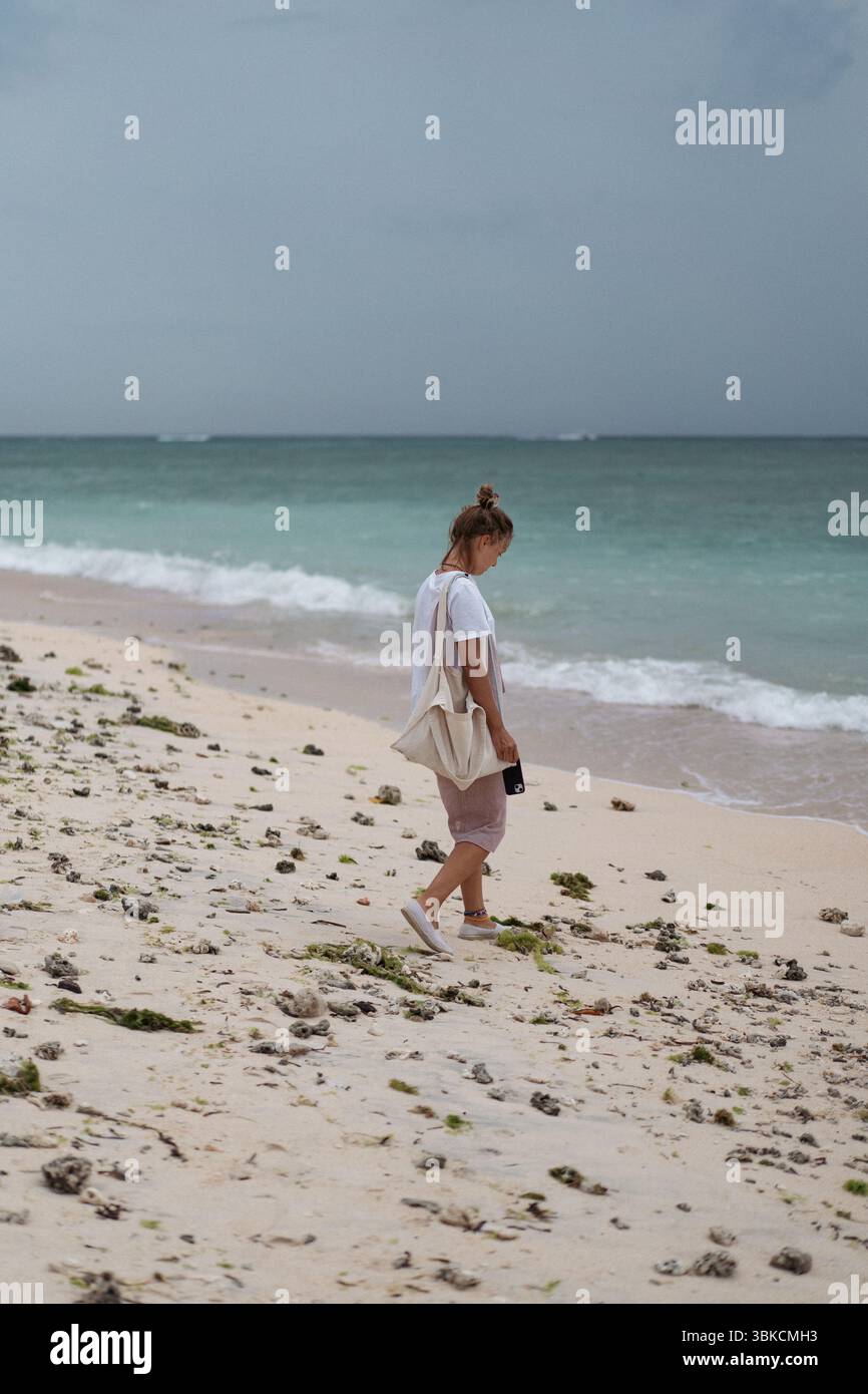 Frau, die allein an einem bewölkten Tag am tropischen Strand spaziert Stockfoto